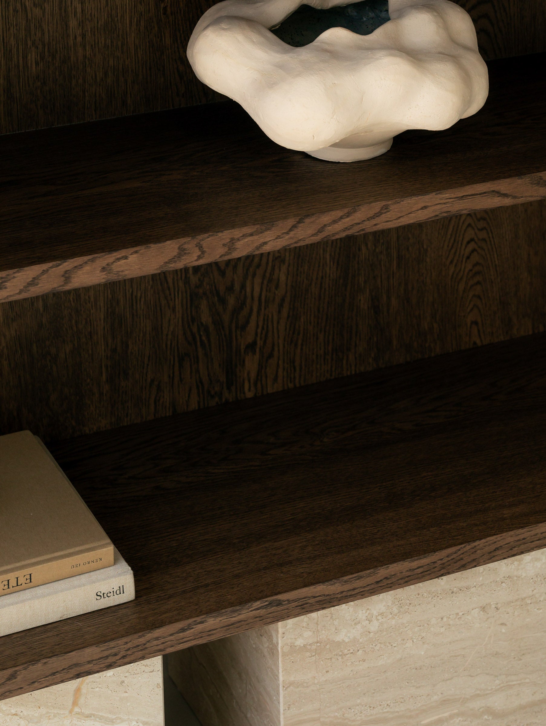 Close-up of a sculptural white ceramic vessel resting on a BLOCK Sideboard  shelf , with stacked photography books below.